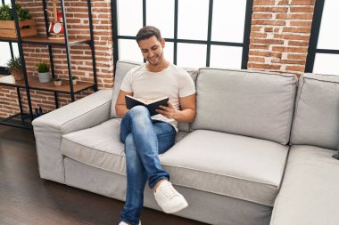 Evdeki kanepede oturmuş kitap okuyan genç bir İspanyol.