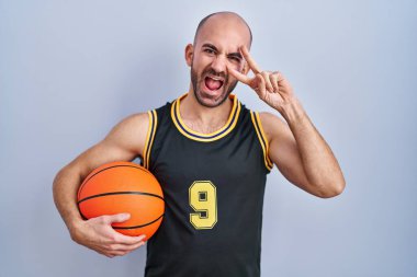 Sakallı, sakallı, basketbol forması giyen, topunu tutan, barış sembolü yapan, parmaklarının üzerinde gülümseyerek zaferi gösteren genç, kel bir adam. 