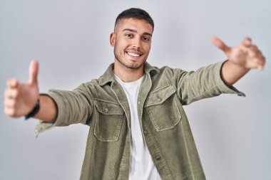 Genç İspanyol bir adam izole edilmiş arka planda durup kameraya bakarak sarılmak için kollarını açmış gülümsüyor. Mutluluğu kucaklayan neşeli bir ifade.. 