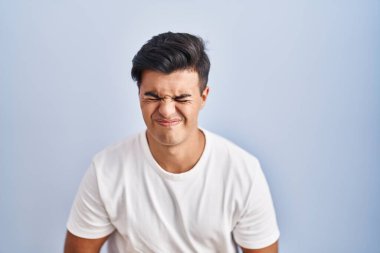 Hispanic man standing over blue background with hand on stomach because indigestion, painful illness feeling unwell. ache concept. 