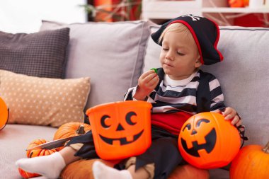 Korsan kostümü giyen sevimli beyaz çocuk evde tatlı yiyor.