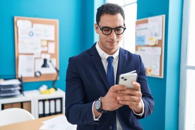 Genç İspanyol iş adamı ofisteki akıllı telefonu kullanarak gülümsüyor.