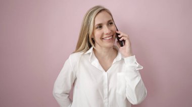 Akıllı telefondan konuşan genç sarışın kadın soyutlanmış pembe arka planda duruyor.