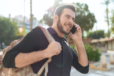 Genç İspanyol adam akıllı telefondan konuşuyor. Sokakta sırt çantası takıyor.