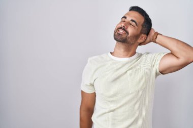 Sakallı İspanyol bir adam izole edilmiş arka planda duruyor. Gülümsüyor, saçlarına dokunuyor, el hareketi yapıyor, çekici ve modaya uygun poz veriyor. 