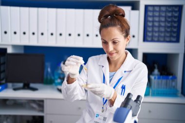 Young woman scientist pouring liquid on sample at laboratory