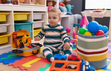 Sevimli beyaz bebek anaokulunda yerde taşaklarıyla oynuyor.