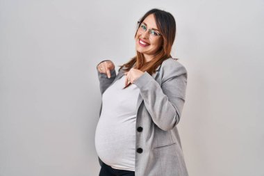 Beyaz arka planda duran hamile bir iş kadını yüzünde bir gülümsemeyle gururla ve mutlu bir şekilde kendini işaret ediyor.. 