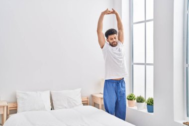 Young arab man waking up stretching arms at bedroom