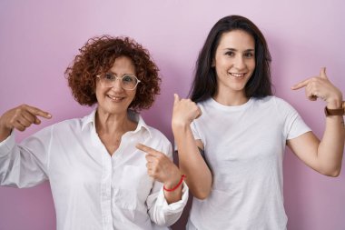 İspanyol anne ve kızı pembe arka planda rahat beyaz t-shirt giyiyorlar. Kendine güveniyorlar. Gülümsüyorlar ve gururlu ve mutlular.. 