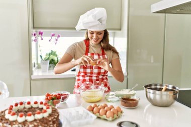 Young beautiful hispanic woman smiling confident pouring egg on bowl at the kitchen