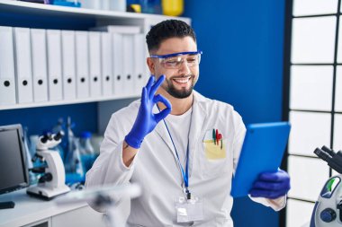 Laboratuvarda çalışan genç yakışıklı adam internette arama yapıyor. Parmaklarıyla imza atıyor, gülümsüyor. Mükemmel bir sembol. 