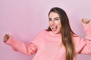 Young hispanic woman standing over pink background dancing happy and cheerful, smiling moving casual and confident listening to music 