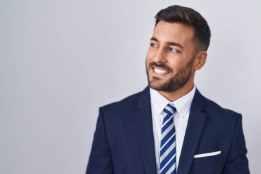 Yakışıklı, takım elbiseli ve kravatlı bir adam yüzünde gülümsemeyle yan yana bakıyor, doğal bir ifade. Kendinden emin gülen. 