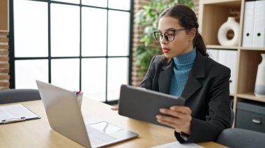 Ofiste dizüstü bilgisayar ve tablet kullanan genç ve güzel İspanyol iş kadını.