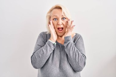 Beyaz arka plan üzerinde duran orta yaşlı beyaz kadın korkmuş ve şok olmuş, şaşırmış ve şaşırmış bir yüz ifadesi var. 
