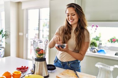 Genç, güzel İspanyol kadın mutfakta sebze suyu ve blender hazırlıyor.