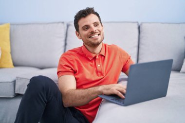 Genç İspanyol adam evde dizüstü bilgisayar kullanıyor.