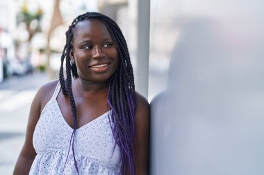 Afro-Amerikalı kadın gülümsüyor. Kendinden emin bir şekilde caddeye bakıyor.