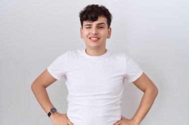 Gündelik beyaz tişört giyen genç bir adam kameraya seksi bir ifadeyle bakıyor, neşeli ve mutlu bir yüzle.. 