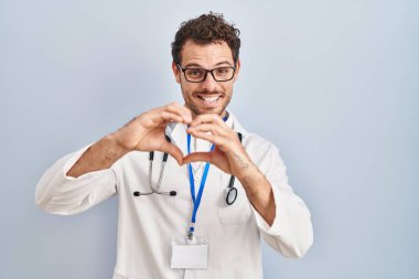 Doktor üniforması ve steteskop giyen genç bir İspanyol, aşkta gülümsüyor ve elleriyle kalp sembolü yapıyor. romantik kavram. 