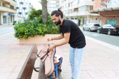 Genç İspanyol müzisyen. Parkta gitar çantası açıyor.