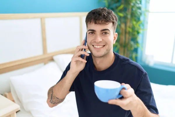 stock image Young hispanic man talking on smartphone drinking coffee at bedroom