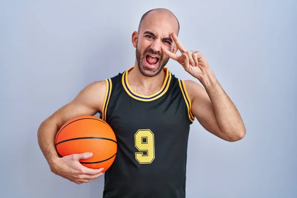 年轻的秃头男子 留着胡子 身穿篮球服 拿着球 手指头捂着脸 笑着表示胜利 — 图库照片