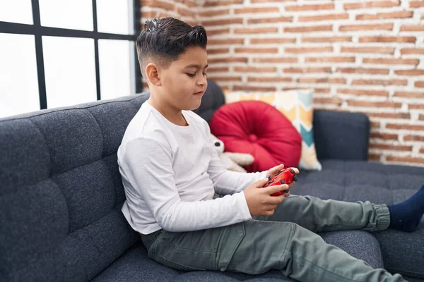 Adorable hispanic boy playing video game sitting on sofa at home
