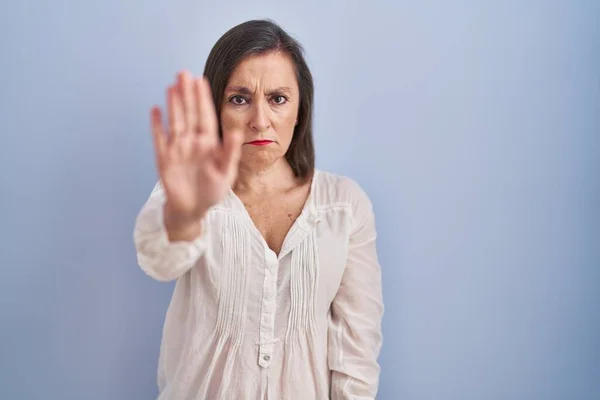 青い背景の上に立っている中年のヒスパニック系の女性は手の手のひらで歌うのを停止します 顔に負の重大なジェスチャーで — ストック写真