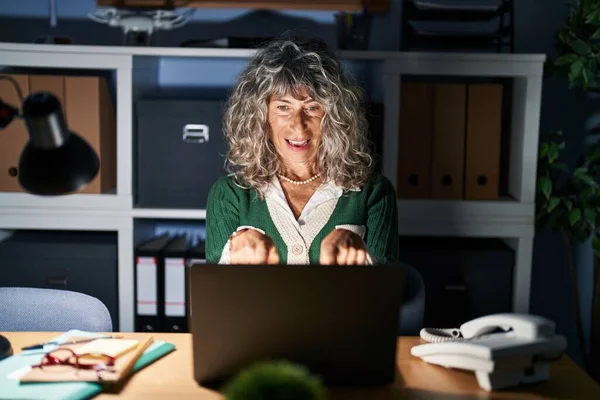 指で指差すコンピューターのノートパソコンとカメラを使って夜勤中の中年女性はポジティブで陽気な笑顔で — ストック写真
