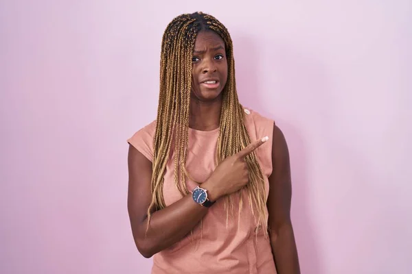Африканская Американка Плетеными Волосами Стоящая Розовом Фоне Указывая Сторону Обеспокоенный — стоковое фото