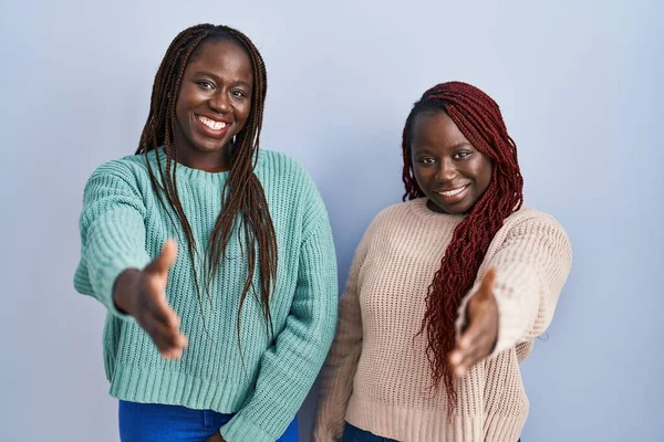 青い背景の上に立っている2人のアフリカ人女性は 挨拶と歓迎として握手を提供しています 成功したビジネス — ストック写真