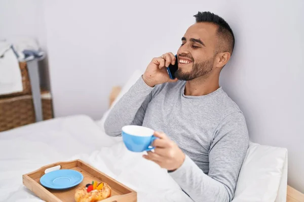 Ung Latinamerikansk Man Pratar Smartphone Äter Frukost Sovrummet — Stockfoto