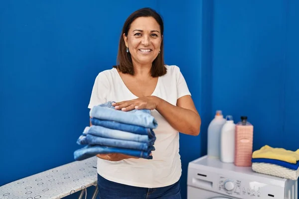 Middle Age Hispanic Woman Smiling Confident Holding Folded Jeans Laundry — 图库照片