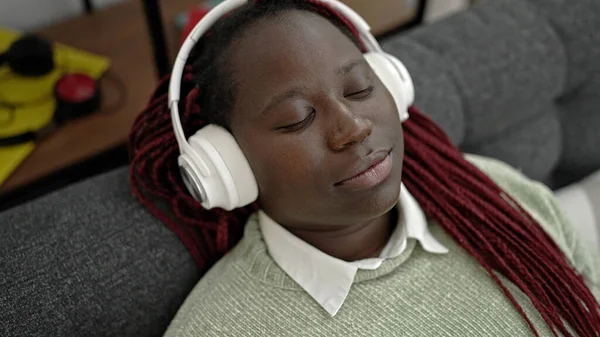 在家里沙发上躺着听音乐的辫子的非洲妇女 — 图库照片