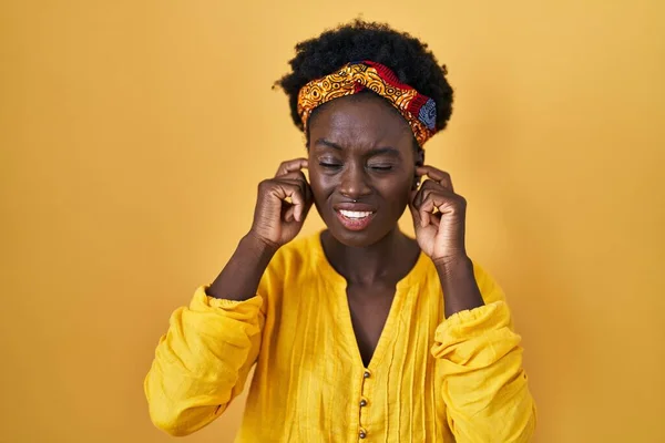 アフリカのターバンを身に着けているアフリカの若い女性は 大きな音楽のノイズに悩まされた表情で指で耳を覆います 聴覚障害の概念 — ストック写真