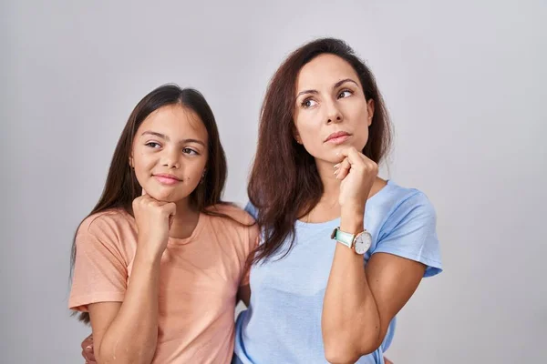 若い母親と娘の白い背景に手をあごの質問については 集中的な表現を考えて立っている 思慮深い顔で笑顔 疑わしい概念 — ストック写真