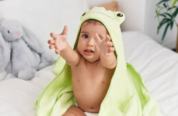 ベッドルームでベッドに座っているカエルタオルを身に着けている愛らしいヒスパニック系の赤ちゃん — ストック写真