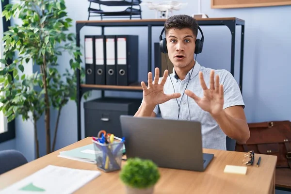 若いヒスパニック系の男は オフィスでは ヘッドフォンを身に着けている手で恐怖表現を停止ジェスチャーを恐れて ショックで叫んで動作します パニックの概念 — ストック写真