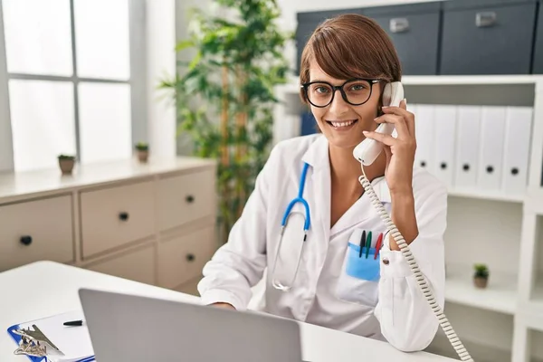 Jovem Bela Mulher Hispânica Médico Usando Laptop Falando Telefone Clínica — Fotografia de Stock