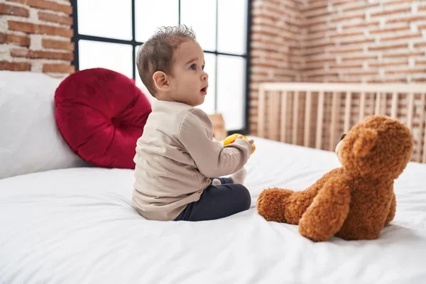 愛らしいHispanic男の子ホールディングアヒルおもちゃ座っています上のベッドルーム — ストック写真