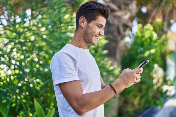 公園でスマートフォンを使って自信を持って笑っている若いヒスパニック系の男 — ストック写真