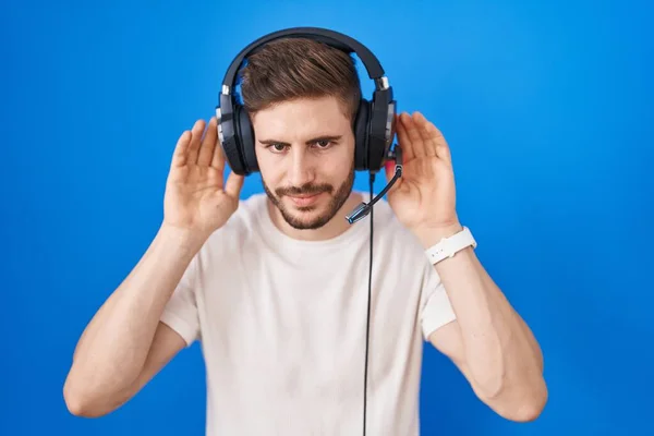Latynos Brodą Słuchający Muzyki Słuchawkach Próbujący Usłyszeć Obie Ręce Uchu — Zdjęcie stockowe