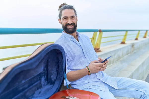Ung Latinamerikansk Man Musiker Med Smartphone Sitter Bänk Vid Havet — Stockfoto