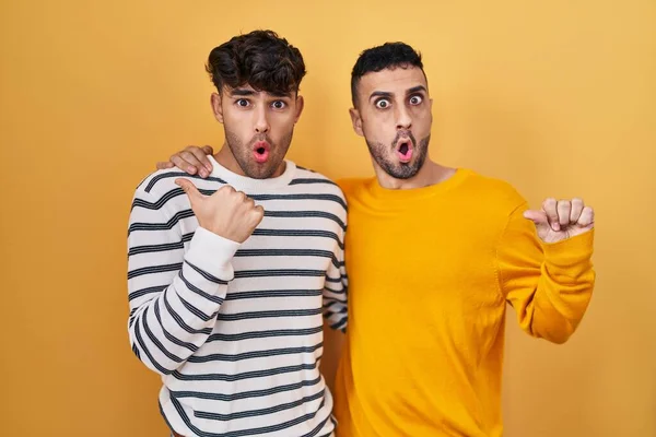 Jong Hispanic Gay Paar Staande Gele Achtergrond Verrast Wijzend Met — Stockfoto
