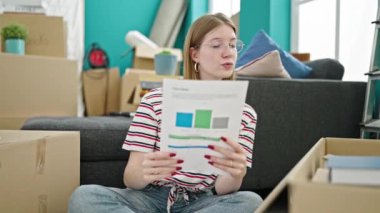 Genç sarışın kadın yeni evdeki karton kağıtları açıyor.