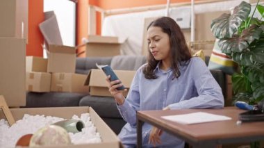 Genç ve güzel İspanyol kadın akıllı telefon kullanıyor. Yeni evinde yerde oturuyor.