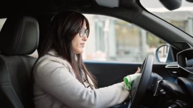 Genç ve güzel İspanyol kadın direksiyonu temizliyor. Sokakta arabada oturuyor.