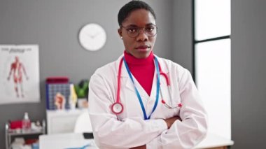 Afro-Amerikalı doktor gülümsüyor. Klinikte kollarını kavuşturup duruyor.